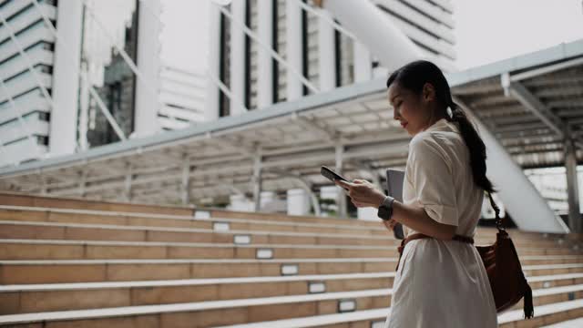 亚洲女性在城市户外行走时用智能手机看屏幕视频素材