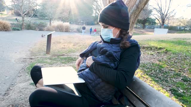 一名在公园工作的成熟女性戴着防护面罩使用笔记本电脑视频素材