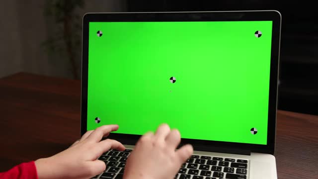 从背影看，男孩坐在桌子上用绿色色度键在笔记本电脑上打字视频素材