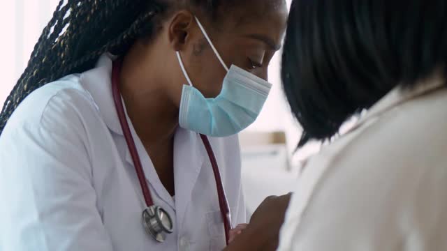 非洲裔儿科女医生在就医时与父母交谈并触摸他们的肩膀，帮助表达同情和鼓励。婴儿病人与母亲在医院就医。医患会诊概念。视频素材