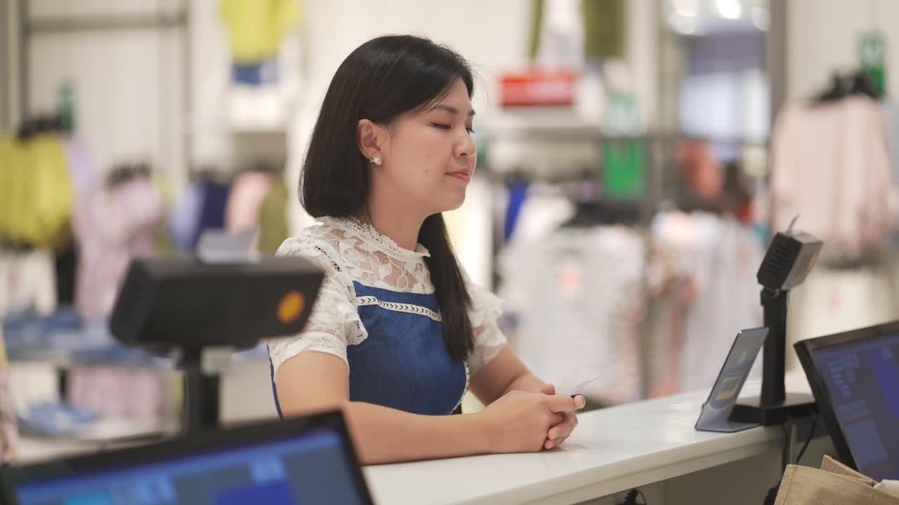 亚洲华人精品店女店主互动与她的客户收银员与信用卡购买结账视频素材
