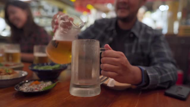一名亚洲男子在日本餐厅为同事倒啤酒视频下载