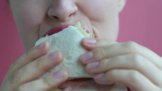 年轻女子吃三明治的特写在粉红色的背景视频素材