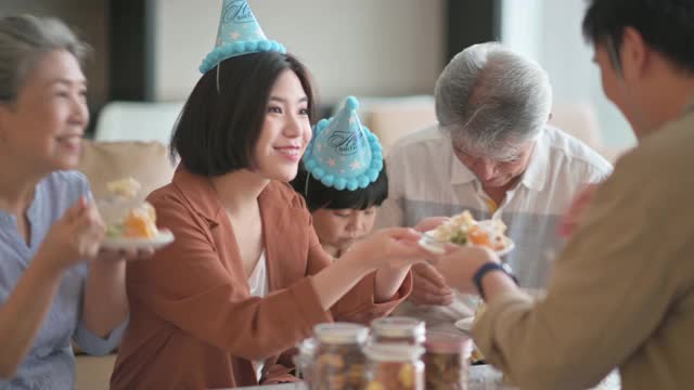 亚洲华人多代同堂庆祝生日，孙子戴着派对帽在客厅吃生日蛋糕视频下载