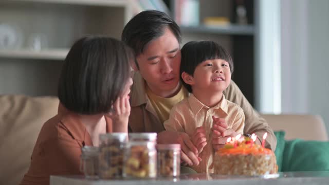 亚洲华人家庭闭上眼睛在生日蛋糕前许下生日愿望，然后在客厅吹生日蜡烛庆祝儿子生日视频下载