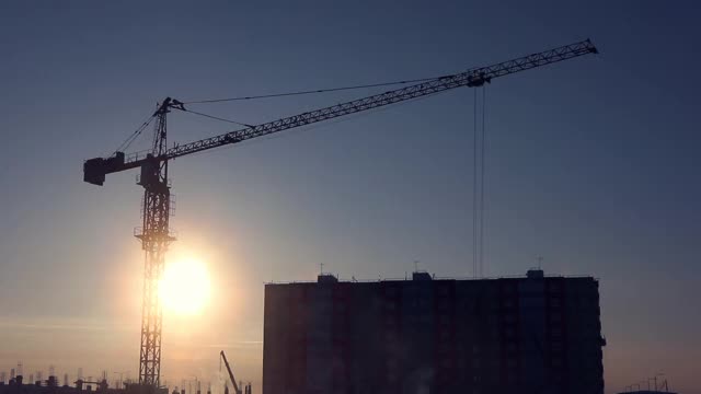 建筑起重机在冬季无云的天空和升起的太阳的背景。视频素材