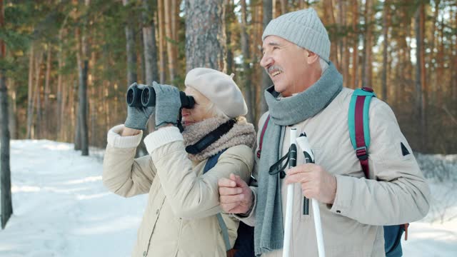 年长的男女游客通过双筒望远镜观看风景，然后在冬季森林滑雪视频下载