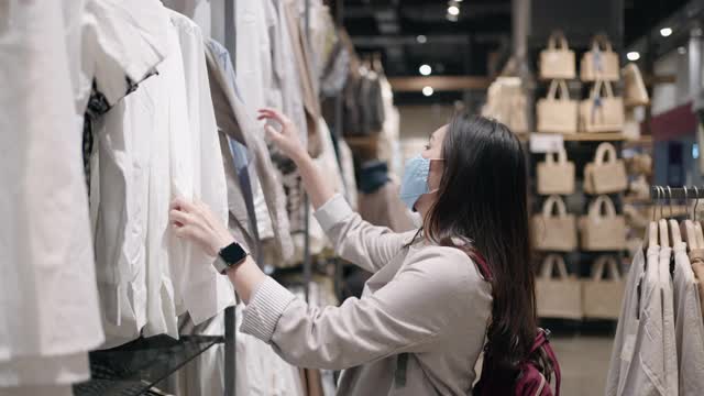 新常态购物，亚洲女性戴口罩在购物中心的服装店购物视频素材