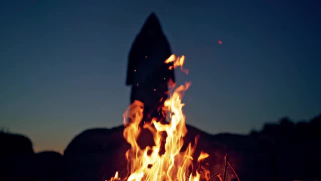 火后面的山上有一个可怕的黑影。橙色的火焰在夜晚和可怕的死亡在黑色斗篷和兜帽挥舞手臂。万圣节的概念。视频素材