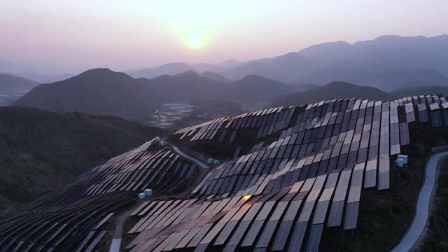 黄昏时分，起伏的山丘上的太阳能发电站鸟瞰图视频下载