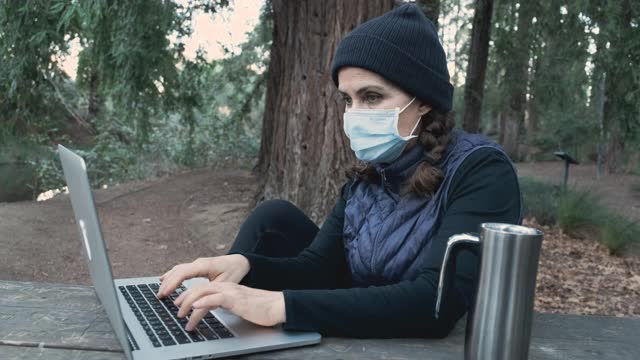 一名在公园工作的成熟女性戴着防护面罩使用笔记本电脑视频素材