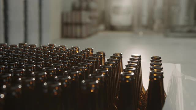 手工工人拿着一个空啤酒瓶在工厂的传送带上生产啤酒。瓶子是焦点。男人的手的特写镜头。生产的概念视频下载
