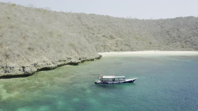 一架飞机从一艘锚定在绿松石海湾的珊瑚礁周围的杂草丛生的山-库塔，印度尼西亚视频下载