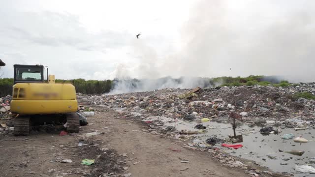 巴厘岛努沙佩尼达和龙目岛，用手持式锁住正在冒烟的垃圾堆，轻微摇晃，黄色拖拉机和腐烂废物的湿池视频素材