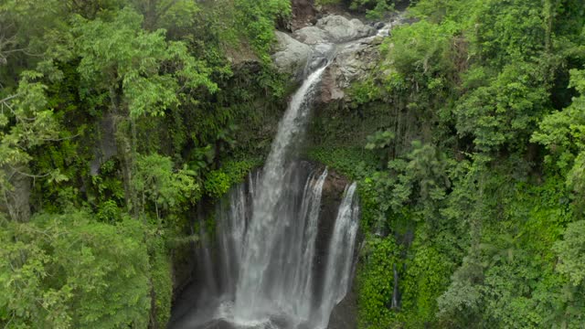 从空中向下进入热带峡谷，一览无间的瀑布被锯齿状的悬崖包围，茂密的树叶覆盖着，凉爽的薄雾从瀑布底部升起——努沙佩尼达&龙目岛，巴厘岛视频下载