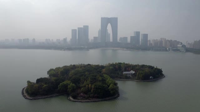 空中拍摄金鸡湖上的绿岛对着摩天大楼，无人机在城市附近飞行对着天空-苏州，中国视频素材