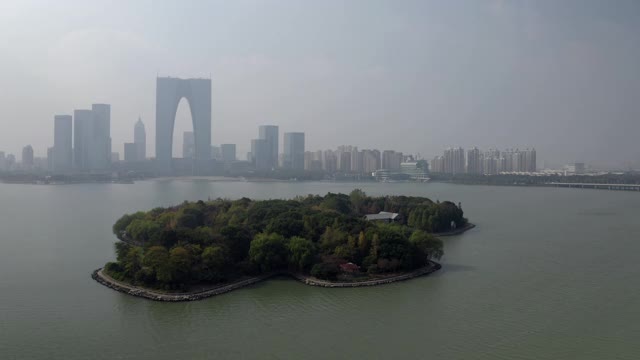 空中摇摄城市附近的金鸡湖上的绿岛，无人机在现代建筑附近飞行——苏州，中国视频素材
