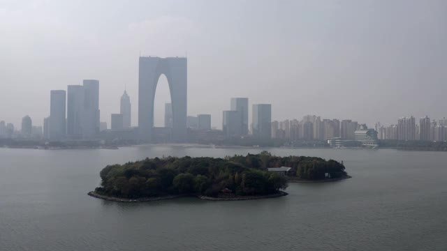 空中拍摄金鸡湖上的树木对着摩天大楼，无人机在城市附近飞行对着天空-苏州，中国视频素材