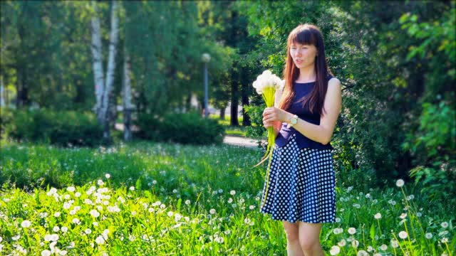 漂亮的女孩站在花圃里。女孩手里拿着一束蓬松的蒲公英。视频下载