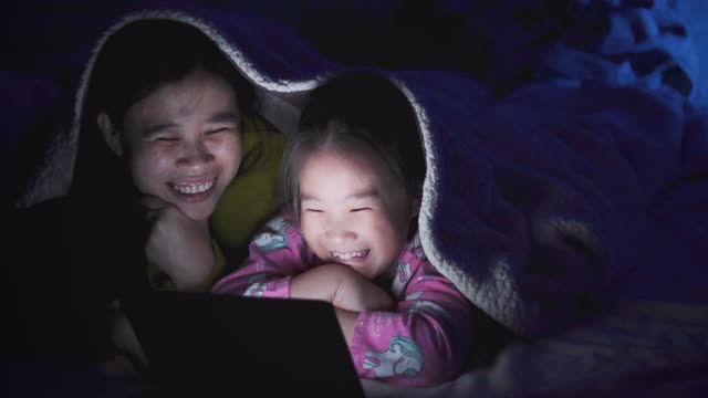 母亲和女儿晚上在卧室看平板电脑视频下载