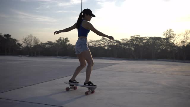 亚洲妇女在美丽的夏天在户外冲浪或滑冰。快乐的年轻女子早上在公园玩冲浪滑冰。视频下载