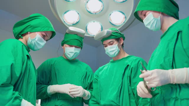 专业的医疗团队在现代化的手术室里进行外科手术。在医院重症监护病人做手术时，亚洲助手向外科医生分发器械。视频素材