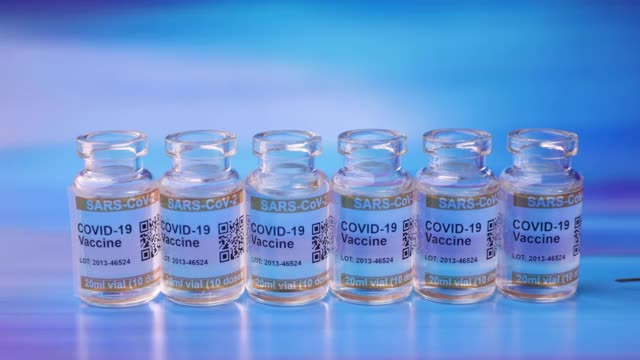蓝色背景是COVID-19疫苗瓶，标记SARS-CoV-2抗冠状病毒。手戴防护手套取注射针筒视频素材