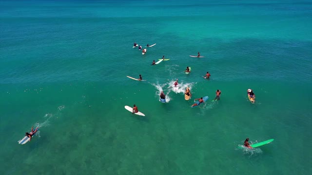 在阳光明媚的日子里，人们在海浪上冲浪时的空中镜头，无人机飞过碧绿的海面上的冲浪者——夏威夷瓦胡岛视频下载