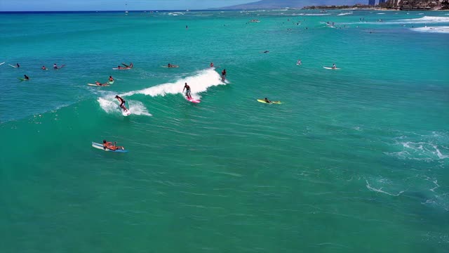 空中慢镜头倾斜拍摄的人冲浪，而溅水在海浪上，无人机飞过冲浪者在晴朗的一天-瓦胡岛，夏威夷视频下载