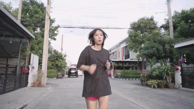 亚洲年轻女性独自在家门口附近的街道上跑步，锻炼动机，流汗，减肥健身运动，节食减肥，控制体重，慢动作视频素材
