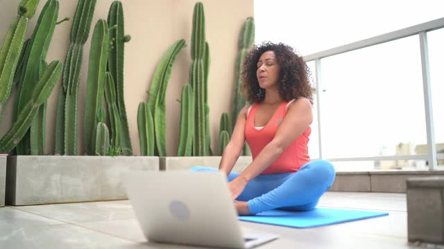 坐在运动垫上使用笔记本电脑的妇女进入在线健身课程视频素材