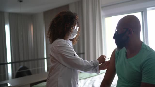 女医生或护士在家为男子接种疫苗-戴口罩视频下载