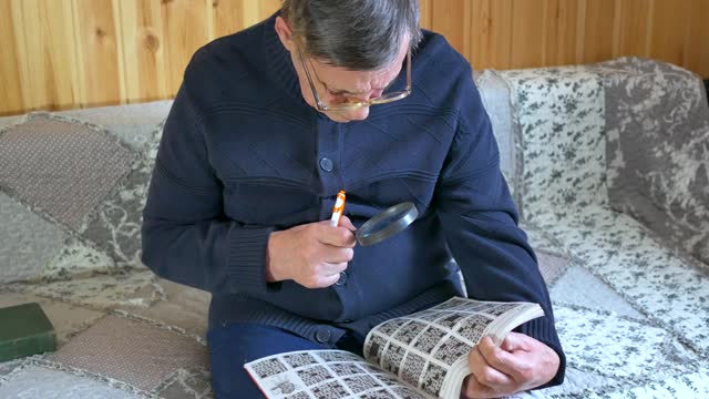 一位戴眼镜的老人正坐在沙发上用钢笔和放大镜写字视频下载