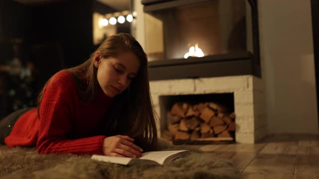 一个十几岁的女孩在壁炉边看书视频素材