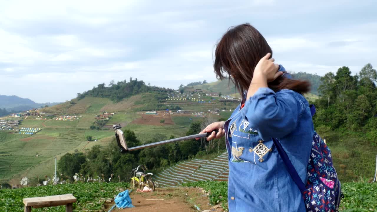 年轻的亚洲女性游客用自拍杆上的智能手机自拍视频下载