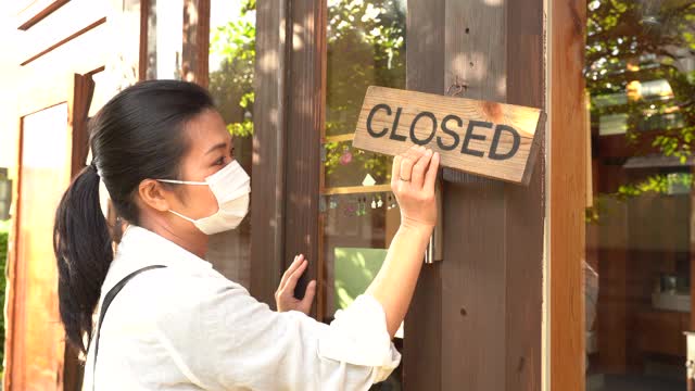 图为一名亚洲餐厅经理戴着口罩，在入口处举着开放标志，为新冠肺炎疫情后重新开业做准备视频下载