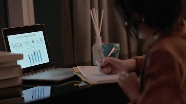 亚洲华人美丽的女人使用笔记本电脑工作，在家自习室书写耳机视频素材