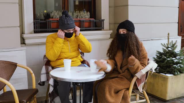 年轻夫妇戴着防护口罩，在餐厅露台上享受美丽的冬日视频素材