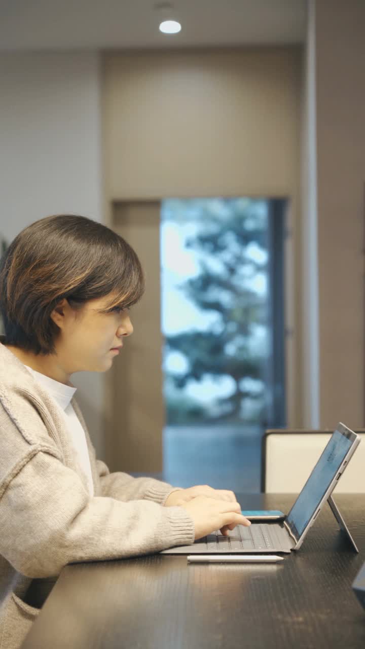 垂直，亚洲女性使用笔记本电脑和智能手机在家里视频素材
