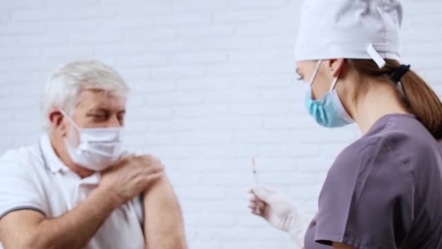 穿著制服的女护士为戴著防护口罩的病人接种疫苗。视频素材