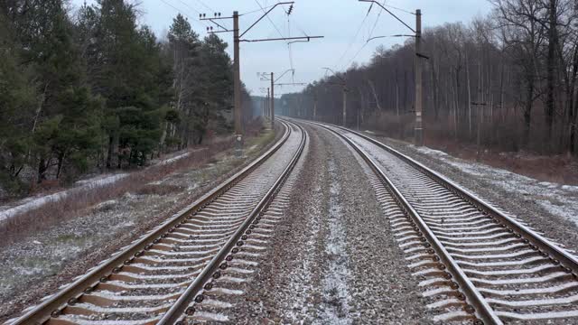 森林里的铁轨上飘着雪花。空中无人机视图。视频素材