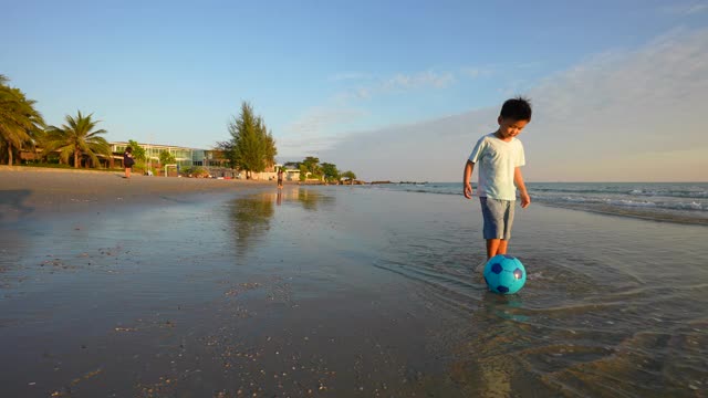 亚洲小孩在沙滩上踢足球。假期和健康的概念视频素材