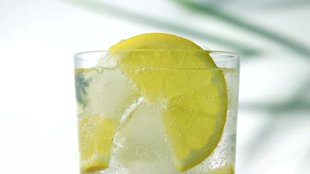 一杯冰水与柠檬片近距离和散焦的绿色棕榈叶在背景视频下载