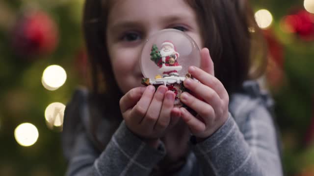 快乐的小女孩微笑着，看着她手里拿着的雪花玻璃球视频下载
