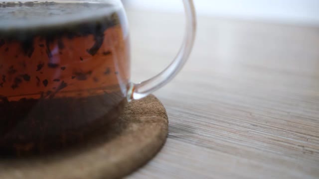 一个玻璃茶壶的特写与冲泡的茶。泡茶的过程，茶道，沸水。叶子漩涡。浓茶。模糊背景4 k视频素材