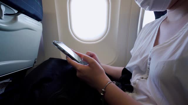 一名年轻女子戴着口罩坐在飞机座位上打电话视频下载