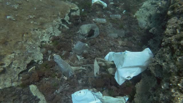 塑料污染，慢镜头，热带鱼游过覆盖着大量塑料垃圾的海底。欧洲地中海海床上的瓶子、袋子和其他塑料碎片。视频素材