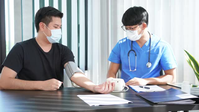 医生戴着防护面罩给病人测量血压并讲解药物治疗的4k视频视频下载