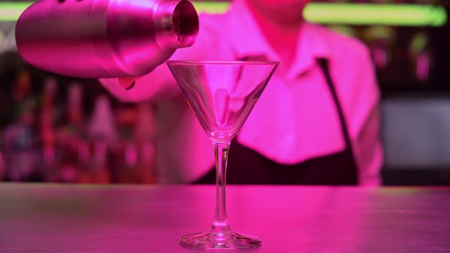 女调酒师将鸡尾酒从摇酒器中倒入玻璃杯视频素材