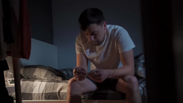 患有严重头痛的人晚上在床上吃药。抑郁的男性坐在床上，服用安眠药或过夜的药物。患有失眠症。担心卧室噩梦的人视频素材